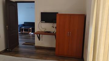Una habitación con un armario de madera, un escritorio con ordenador y una televisión en la pared.