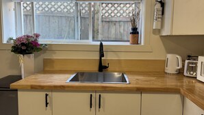 A kitchen with a wooden countertop, a stainless steel sink, a window with a view of a wooden fence, and a potted plant with flowers. - Cedar-Cottage Comfort Suite (Vancouver)
