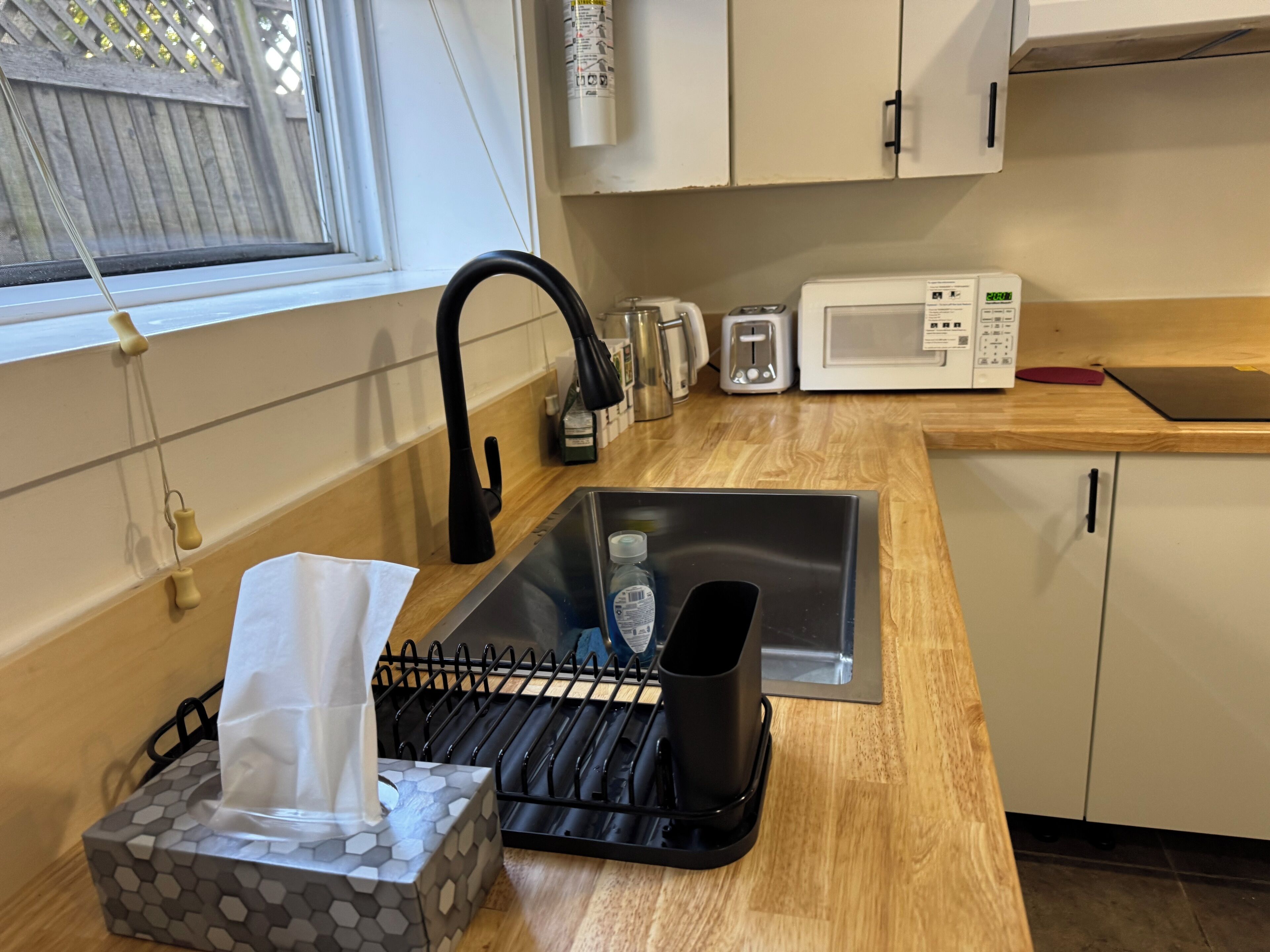 A kitchen with a sink, a microwave, and a window with a view of a wooden fence.