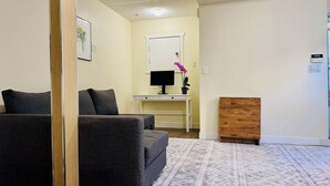 A living room with a sofa, a small table with a monitor, a wooden cabinet, and a patterned rug. - Cedar-Cottage Comfort Suite (Vancouver)