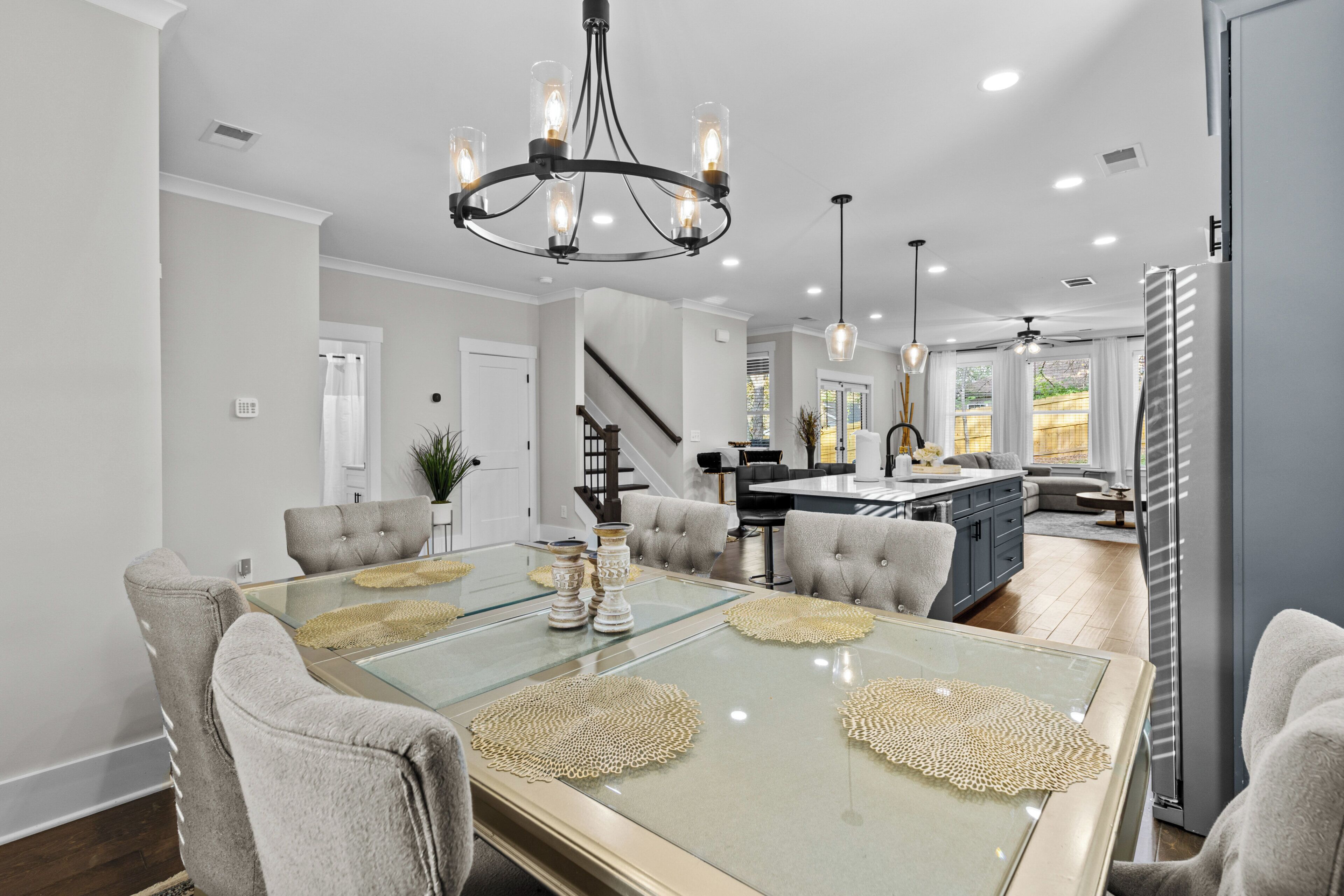A modern dining area with a glass table, grey upholstered chairs, and a chandelier.