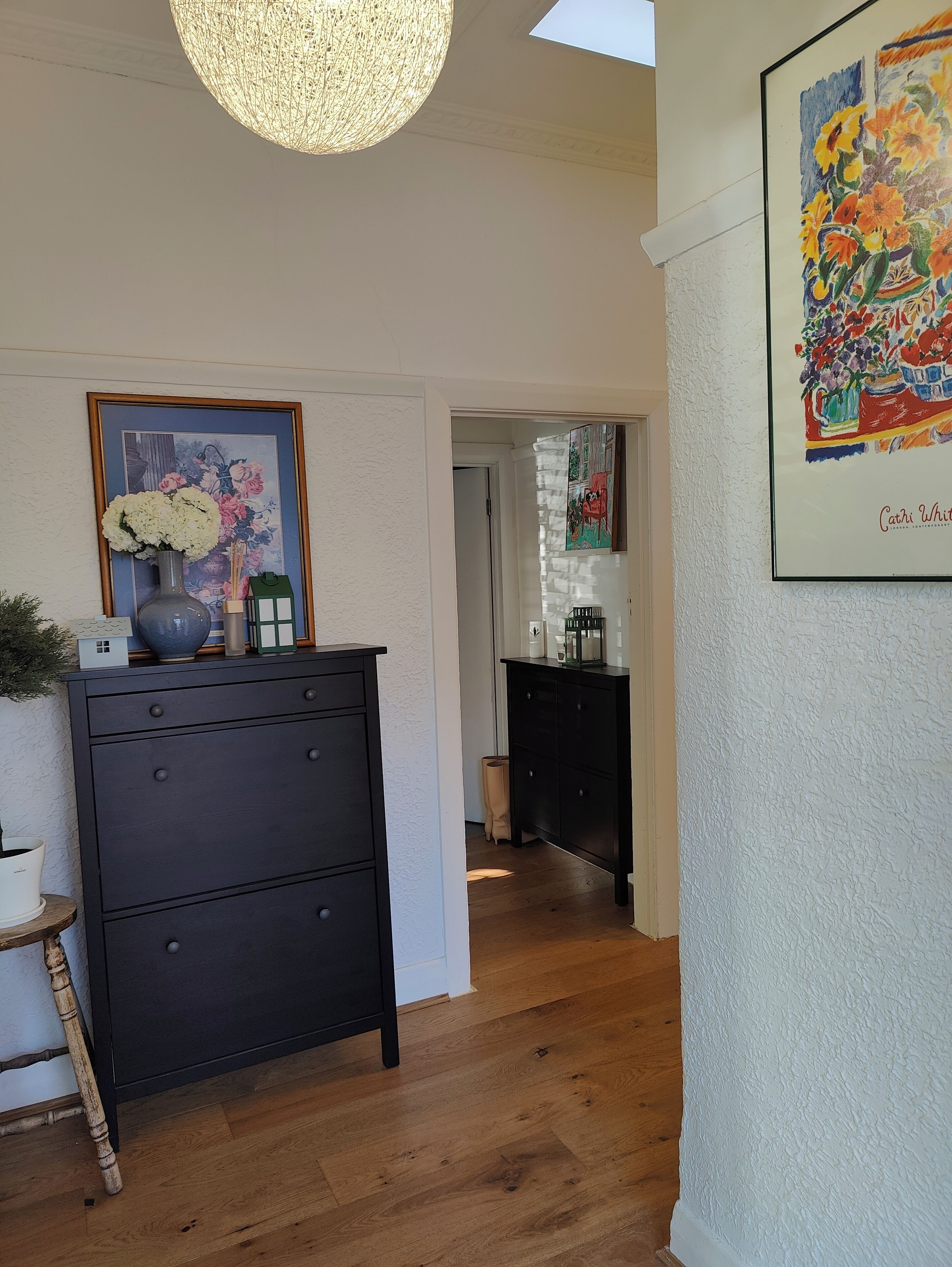 Un couloir avec une commode en bois foncé, un tableau floral encadré et un luminaire au plafond.