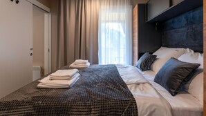 Une chambre d’hôtel moderne avec un grand lit, une tête de lit et une vue sur l’extérieur à travers des rideaux transparents.
