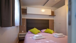 Ein Schlafzimmer mit einem Bett, Kissen, einem Nachttisch, einem Kleiderschrank und einem fest eingebauten Regal über dem Bett.