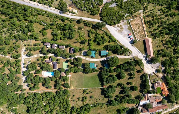 An aerial view of a residential area with multiple houses, a swimming pool, and a large open field.