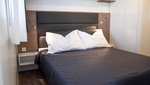 A neatly made bed with a dark headboard and white pillows, a bedside table with a lamp, and a wooden floor. - Awesome (sta)caravan in Obrovac with WiFi (Obrovac)