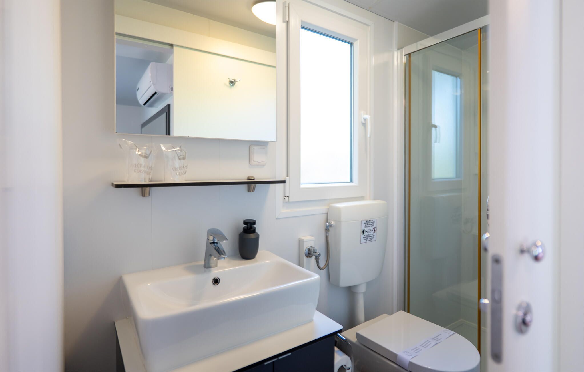 A modern bathroom with a white sink, a mirror, a glass shower enclosure, and a toilet.