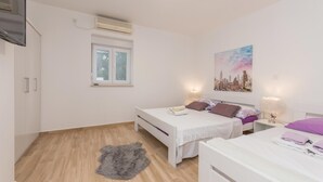 Un dormitorio con dos camas, una ventana, un equipo de aire acondicionado y un cuadro de un paisaje urbano.