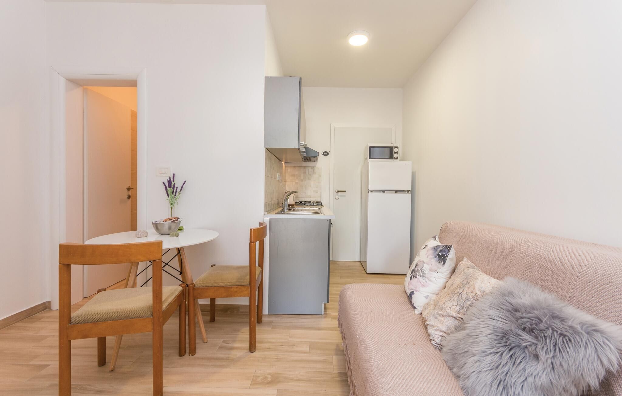 Un espacio habitable compacto con kitchenette, una zona de comedor con mesa y sillas, y un sofá con un almohadón mullido.
