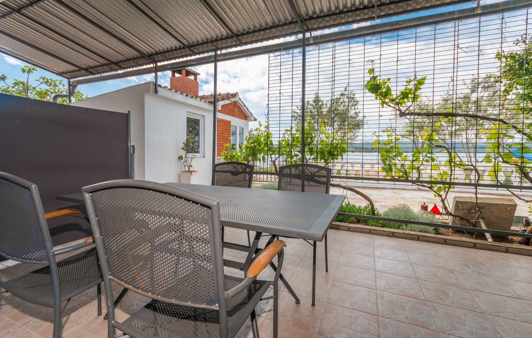 An outdoor patio with a table and chairs, a view of the sea, and a building in the background.
