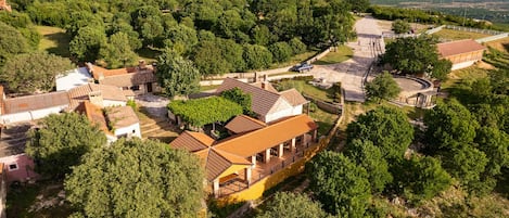 Un village rural doté d’une architecture traditionnelle, avec des bâtiments aux toits de tuiles et des murs en pierre, entouré d’une végétation luxuriante et bordé de montagnes en arrière-plan.