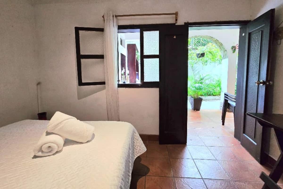 A bedroom with a bed, a window, and an open door leading outside.