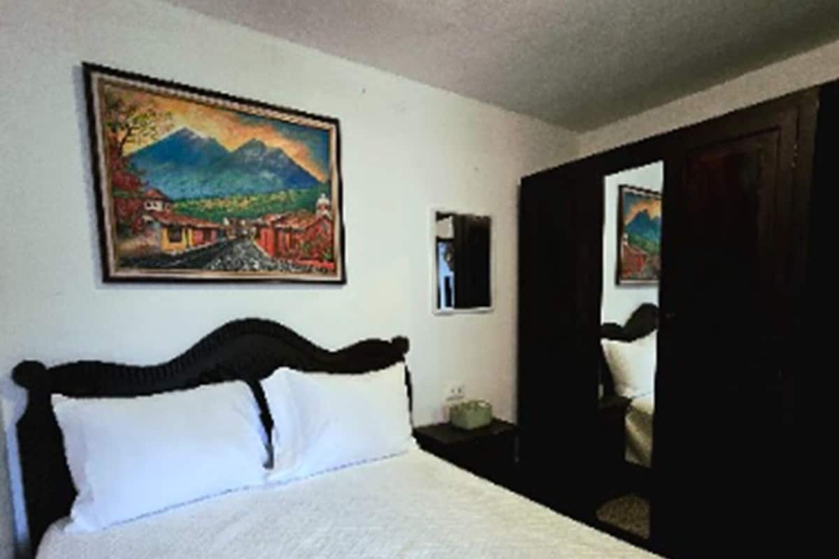 A bedroom with a bed, a painting on the wall, and a mirror.