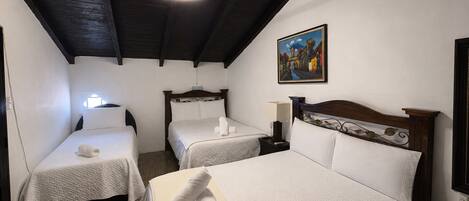 Ein Hotelzimmer mit zwei Einzelbetten, einem großen Bett, Holzbalkendecke, einem Gemälde an der Wand und einer Deckenleuchte.