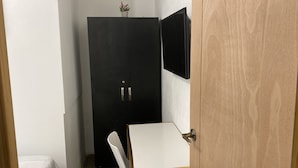Una habitació amb un armari negre, un escriptori blanc i una petita planta en test sobre l'armari.