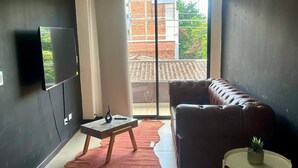 Ett modernt vardagsrum med en soffa i läder, ett litet bord, en tv som är monterad på väggen och en skjutdörr i glas som leder ut till en balkong.