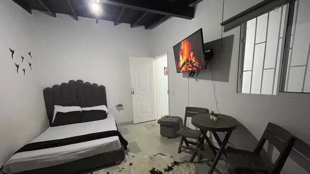 Une chambre à coucher avec un lit, un téléviseur fixé au mur, une petite table avec des chaises et un tapis en peau de vache.
