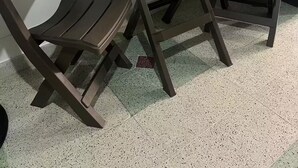 Une petite table en bois sombre, sur laquelle est posée une seule plante en pot, est flanquée de deux chaises assorties, dans une pièce dont le sol est carrelé et qui possède une fenêtre avec des stores.