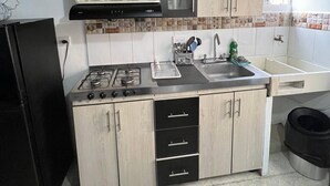 Une cuisine de taille réduite, équipée d’une cuisinière à gaz, d’un évier et de meubles de rangement en bois.