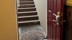 A red door with a metal handle and a keyhole, leading to a staircase with a metal grate at the bottom. - Alaska Tucked Inn-The Den ; Cozy 1 bedroom with all the touches of home! (Fairbanks)