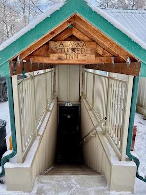 Een houten gebouw met de naam 'Alaska Tucked Inn', voorzien van een met sneeuw bedekte dak en een deur bij de ingang.