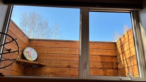 A room with a large window, wooden walls, and a clock on the wall. - Alaska Tucked Inn-The Den ; Cozy 1 bedroom with all the touches of home! (Fairbanks)