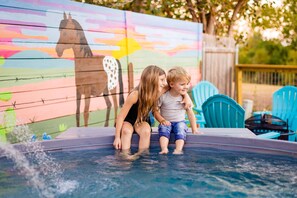 Deux enfants sont assis dans un jacuzzi, avec une fresque colorée en arrière-plan.