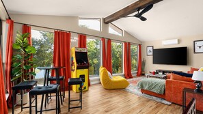 Een ruime woonkamer met een groot raam, een gameconsole, een televisie en een gezellige zithoek.