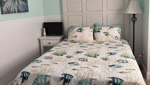 Quarto com cama, mesa de cabeceira, abajur e um quadro na parede.
