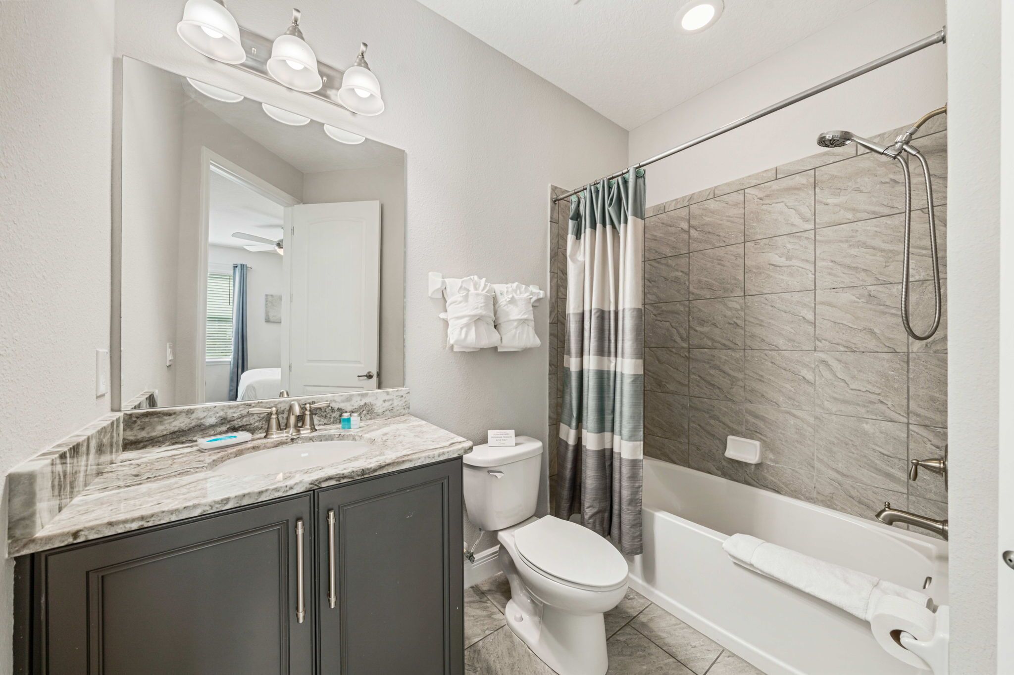 A modern bathroom with a marble countertop, a toilet, a shower with a curtain, and a bathtub.
