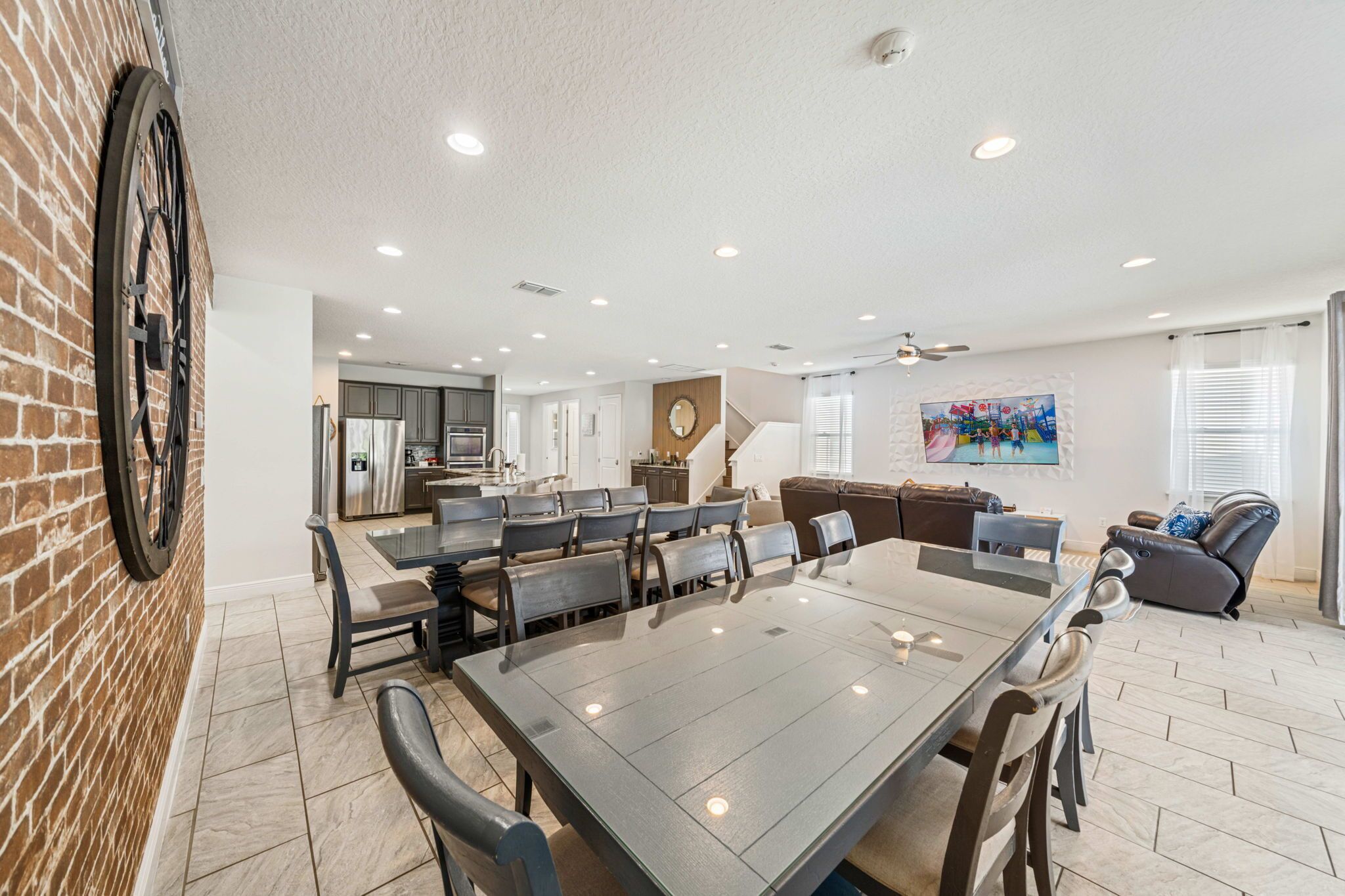 A spacious living room with a large dining table, a fireplace, and a kitchen in the background.