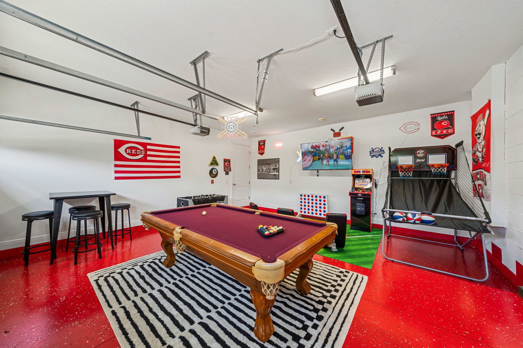 Una mesa de billar con superficie de fieltro rojo, una vara de billar y un juego de taburetes.