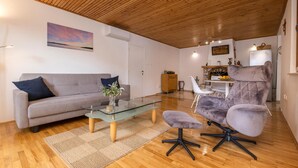 Un salon moderne avec un plafond en bois, un canapé gris, une table basse en verre et un fauteuil gris.