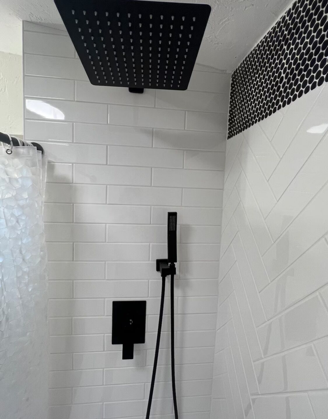 Un espace douche équipé d’un grand pommeau de douche noir, d’un pommeau de douche à main et d’un panneau de commande mural.