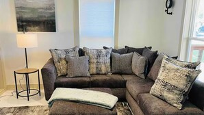 Un divano componibile con cuscini decorati, un tavolino rotondo, una lampada da terra e un quadro appeso al muro.