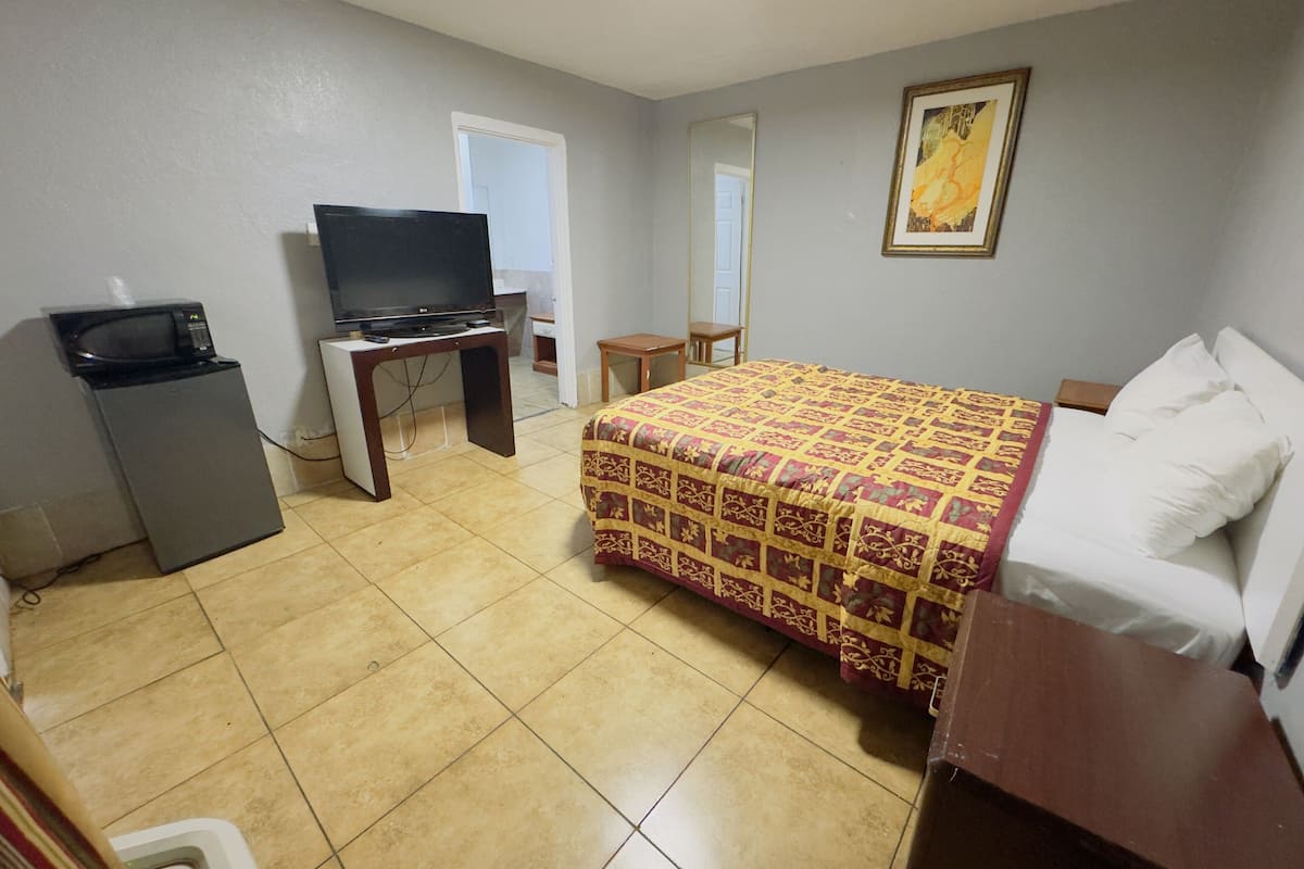 A hotel room with a bed, a television, a desk, and a small refrigerator.