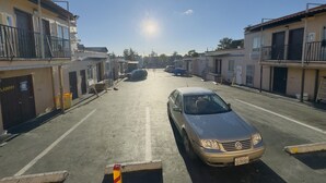 A street view with a parked car, buildings with balconies, and a clear sky. - Parklane Motel (Oakland)