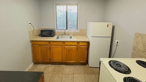 A compact kitchen with wooden cabinets, a white refrigerator, a microwave, and a stove. - Parklane Motel (Oakland)