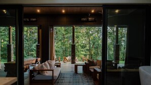 A modern interior with a large glass door leading to a forested outdoor area, furnished with sofas and a fireplace. - Swanky Chalet with Sauna, HotTub, EpicView, Golf, King Suite (Blue Ridge)