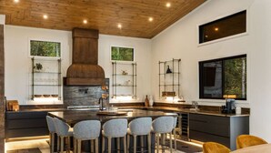 A modern kitchen with a central island, bar stools, and a large window. - Swanky Chalet with Sauna, HotTub, EpicView, Golf, King Suite (Blue Ridge)