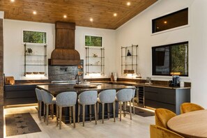 A modern kitchen with a central island, bar stools, and a large window. - Swanky Chalet with Sauna, HotTub, EpicView, Golf, King Suite (Blue Ridge)