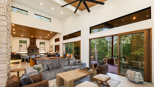 A spacious living area with a large sofa, coffee table, and a view of the outdoors through large sliding doors. - Swanky Chalet with Sauna, HotTub, EpicView, Golf, King Suite (Blue Ridge)