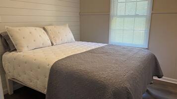 A bedroom with a bed, two pillows, a window with blinds, and a wooden wall.