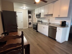 A compact kitchen with white cabinets, a microwave, oven, and dishwasher. There is a dining table with chairs and a washing machine in the background. - Convenient 2BR -1.5 bath near Lee University, Chattanooga airport, Ocoee River (Cleveland)