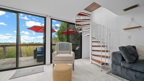A modern living room with a spiral staircase, a sofa, a chair, and a view of the outdoors. - B1 - Riverview Bungalow (Crystal River)