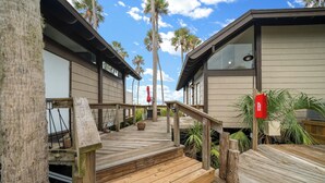 A wooden deck leading to a building with a red mailbox, surrounded by palm trees and potted plants. - B1 - Riverview Bungalow (Crystal River)