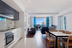 Une cuisine moderne dotée d’appareils électroménagers intégrés, un coin repas avec une table et des chaises, et une vue sur la ville grâce à de grandes fenêtres.