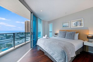 A hotel room with a large bed, a bedside table with a lamp, and a view of the city through floor-to-ceiling windows. - Deluxe Two Bedroom Hilton Apartment (Surfers Paradise)