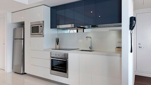 Eine moderne Küche mit weißen Schränken, einem Edelstahl-Kühlschrank, einer Mikrowelle, einem Backofen und einem Spülbecken mit Armatur.
