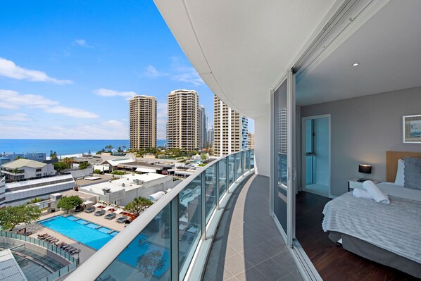 Un balcon avec une piscine, une chambre avec un lit et une vue sur les gratte-ciel et l’océan.